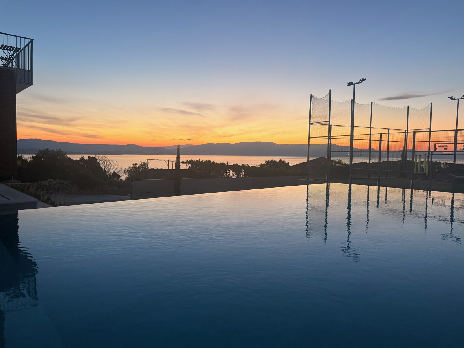 Infinitypool ved solopgang med padelbanerne og havet i baggrunden